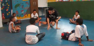 professor de dança ensina movimento de break para crianças sentadas no chão