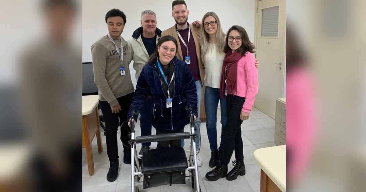 mulher com paralisia cerebral se apoia em cadeira de rodas cercada por colegas de trabalho